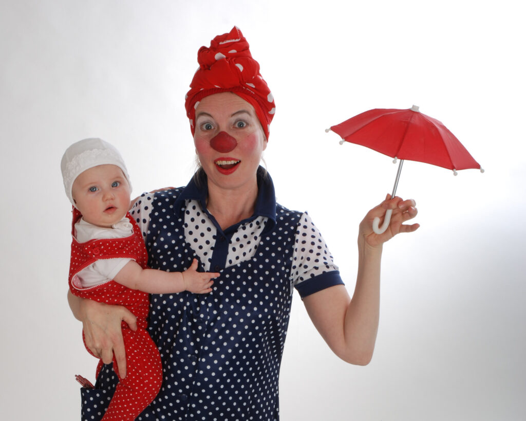 Clownen Loppa håller i ett barn på höften och ett litet rött paraply i den andra handen.