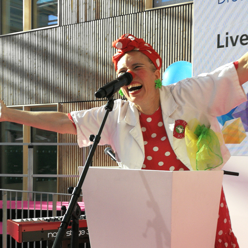 Clownen Loppa står framför mikrofon med leende och armarna utsträckta upp i luften